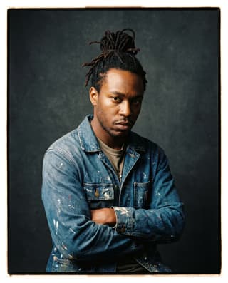 Studio portrait of a painter in a paint-flecked work jacket.