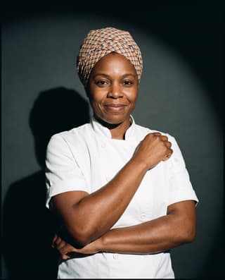 Studio portrait of a chef in a white coat and printed head wrap.