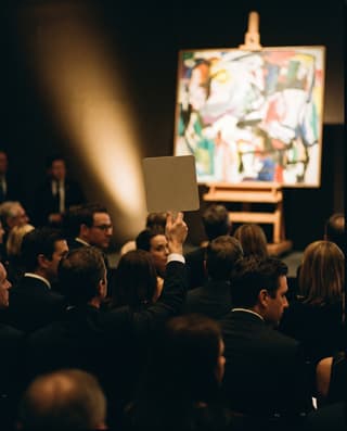 A single raised bidding paddle in a dark, crowded auction room.