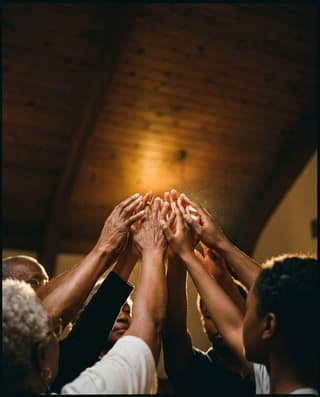 Many hands raised together in warm low light.